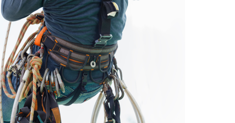 Mężczyzna wisi na linie na szkoleniu IRATA. Do uprzęży przyczepione ma środki ochrony indywidualnej.