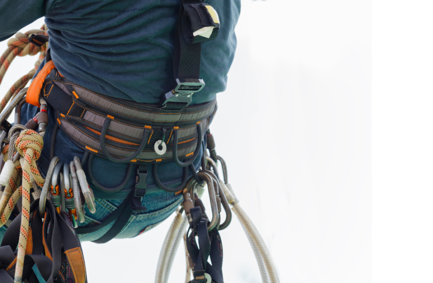 Mężczyzna wisi na linie na szkoleniu IRATA. Do uprzęży przyczepione ma środki ochrony indywidualnej.
